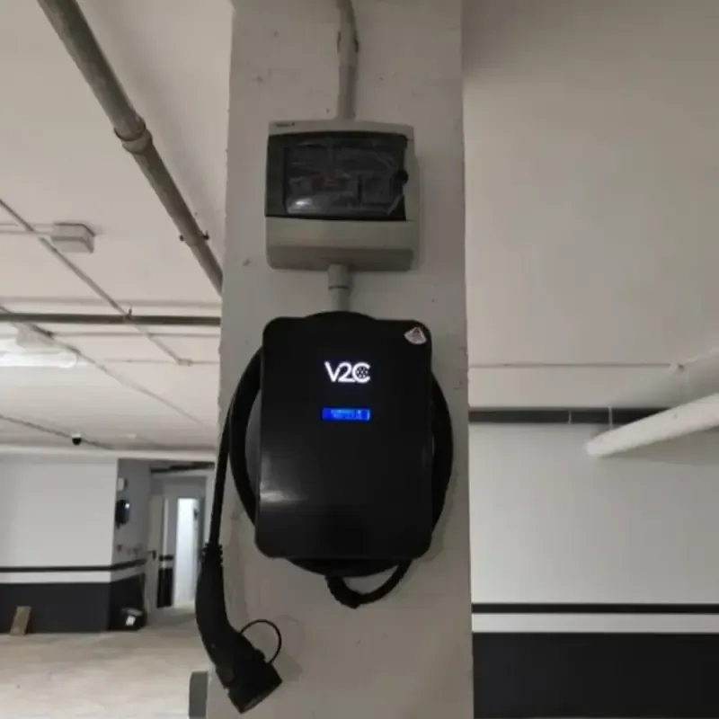 Estación de carga para vehículos eléctricos V2C montada sobre un pilar de hormigón en un aparcamiento.