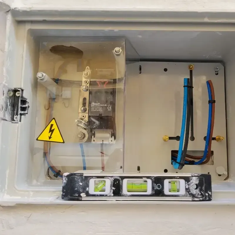 Panel eléctrico abierto con cableado, caja de disyuntores y señal amarilla de advertencia de alto voltaje.