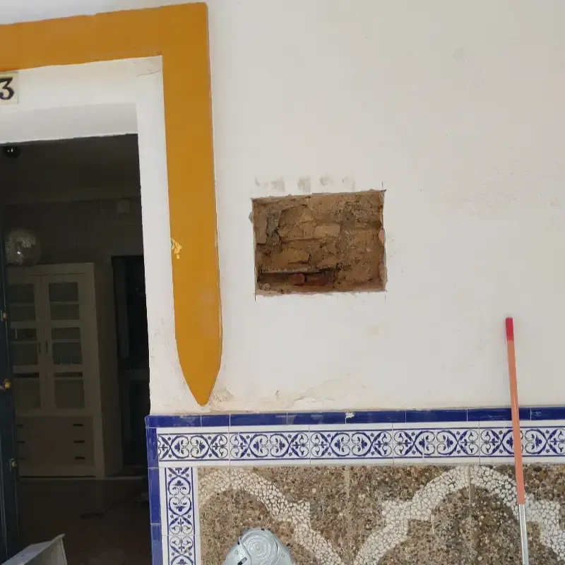 Pared blanca con una puerta con marco amarillo, un parche de ladrillo visto y un revestimiento de azulejos.