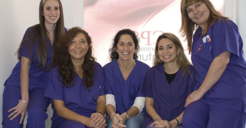 Cinco personas vestidas con uniformes morados, sonriendo, posando juntas en el interior.