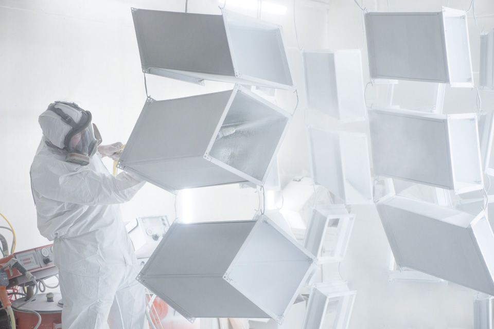 Une personne portant un équipement de protection peint à la bombe des formes géométriques blanches dans une cabine de peinture blanche.