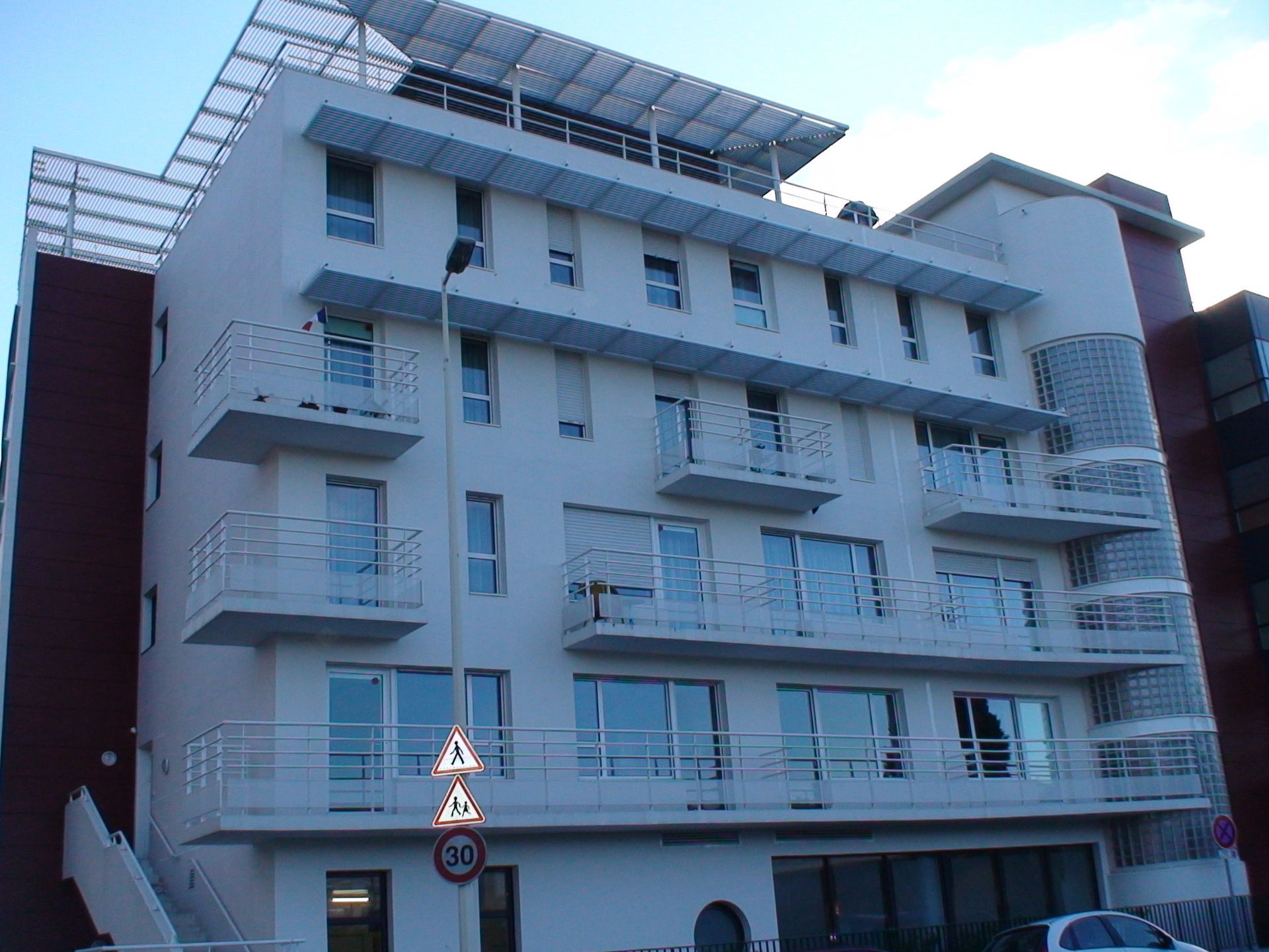 Bâtiment blanc moderne avec balcons et panneaux solaires sur le toit.