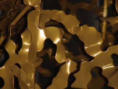 Sculpture abstraite en métal doré aux formes organiques et fluides, reflétant la lumière.