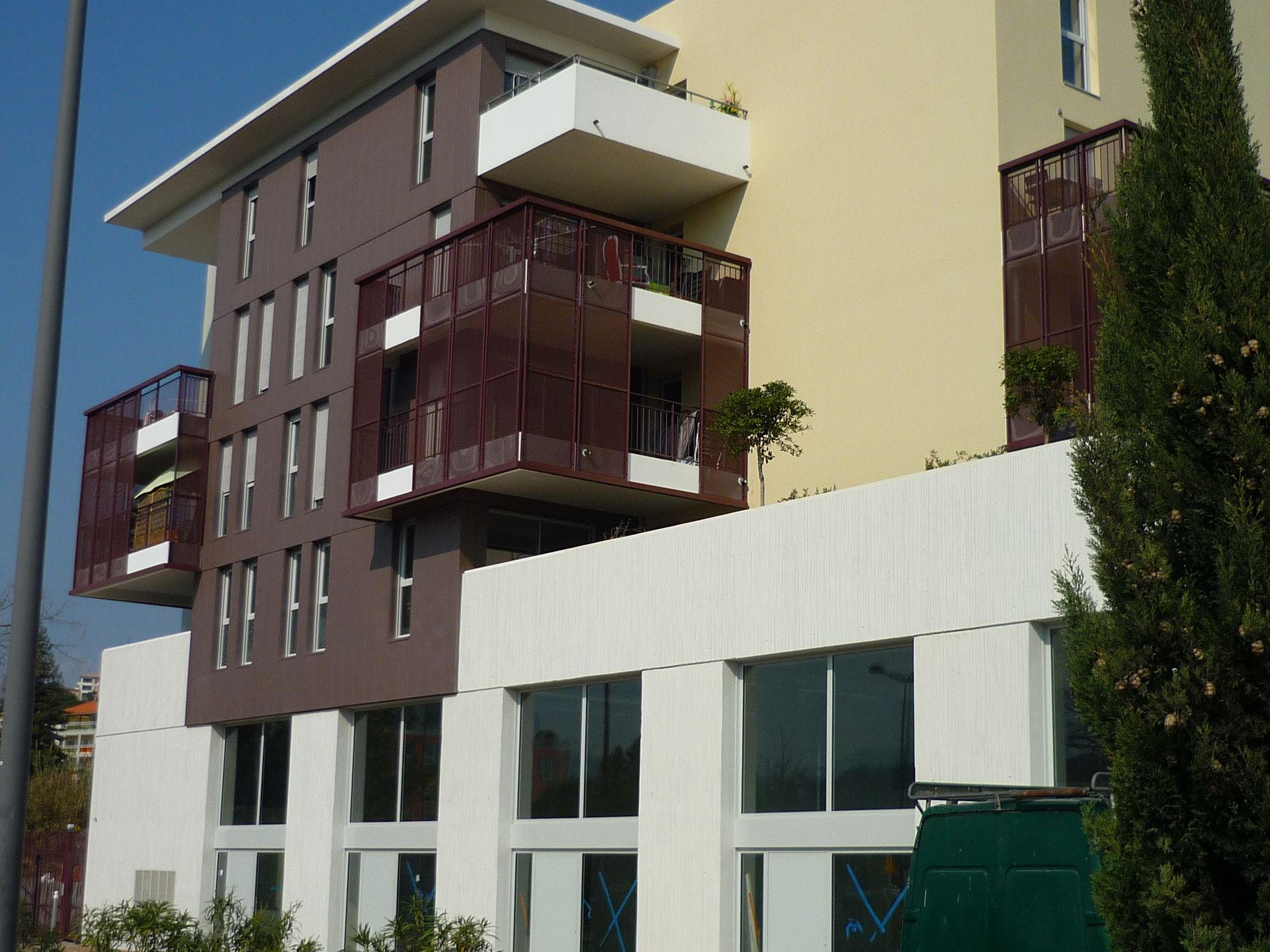 Immeuble d'appartements moderne avec façade marron et beige, balcons et grandes fenêtres.