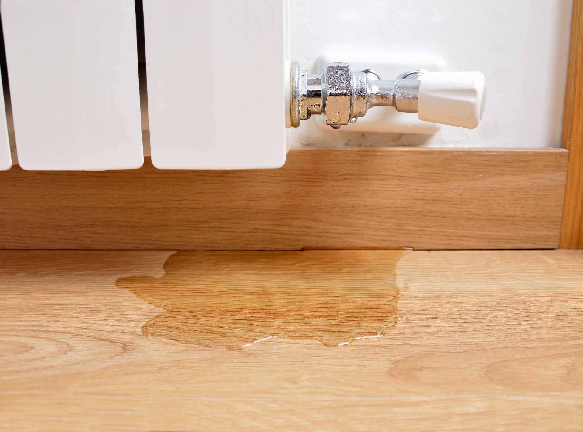 Flaque d'eau sur un parquet à cause d'une fuite sur un radiateur