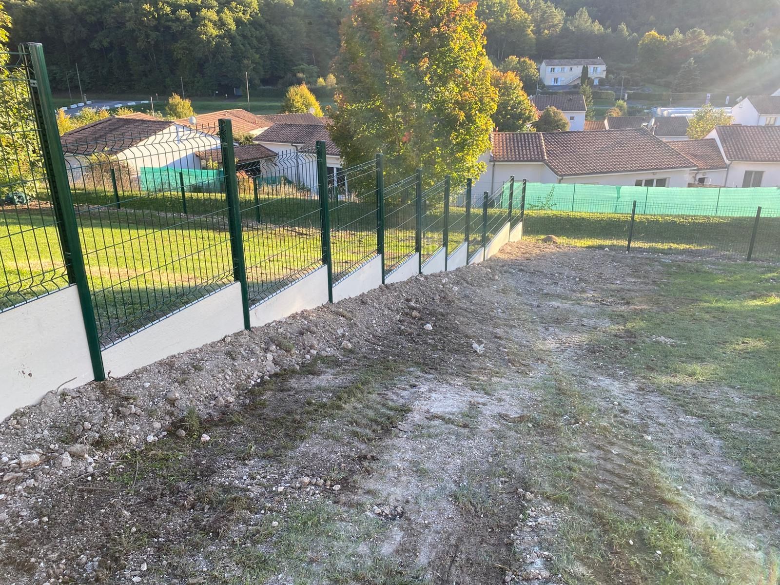 Une clôture en grillage vert à flanc de colline, avec du ciment blanc à sa base. 