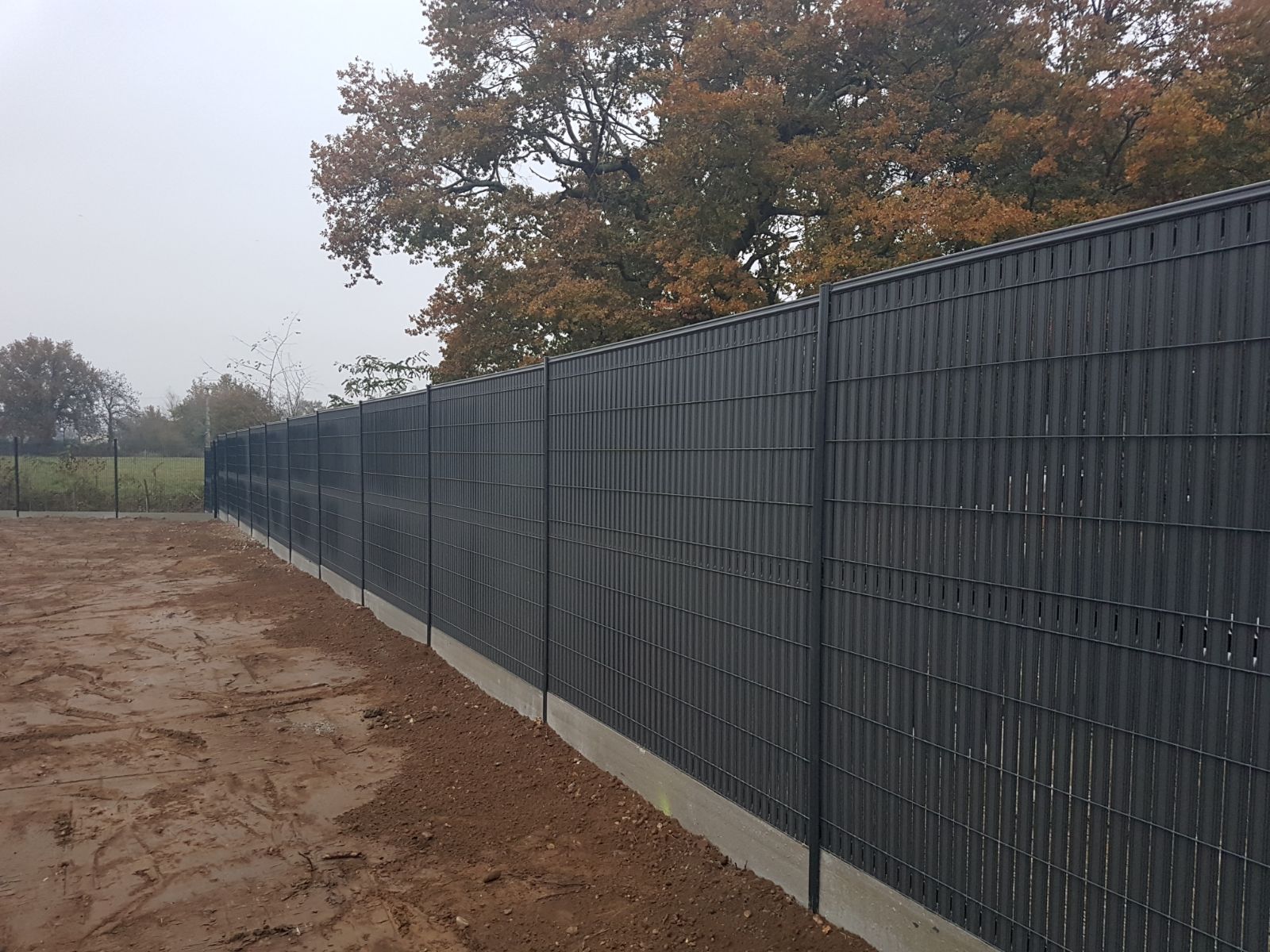 Clôture noire assurant l'intimité le long d'un terrain vague.