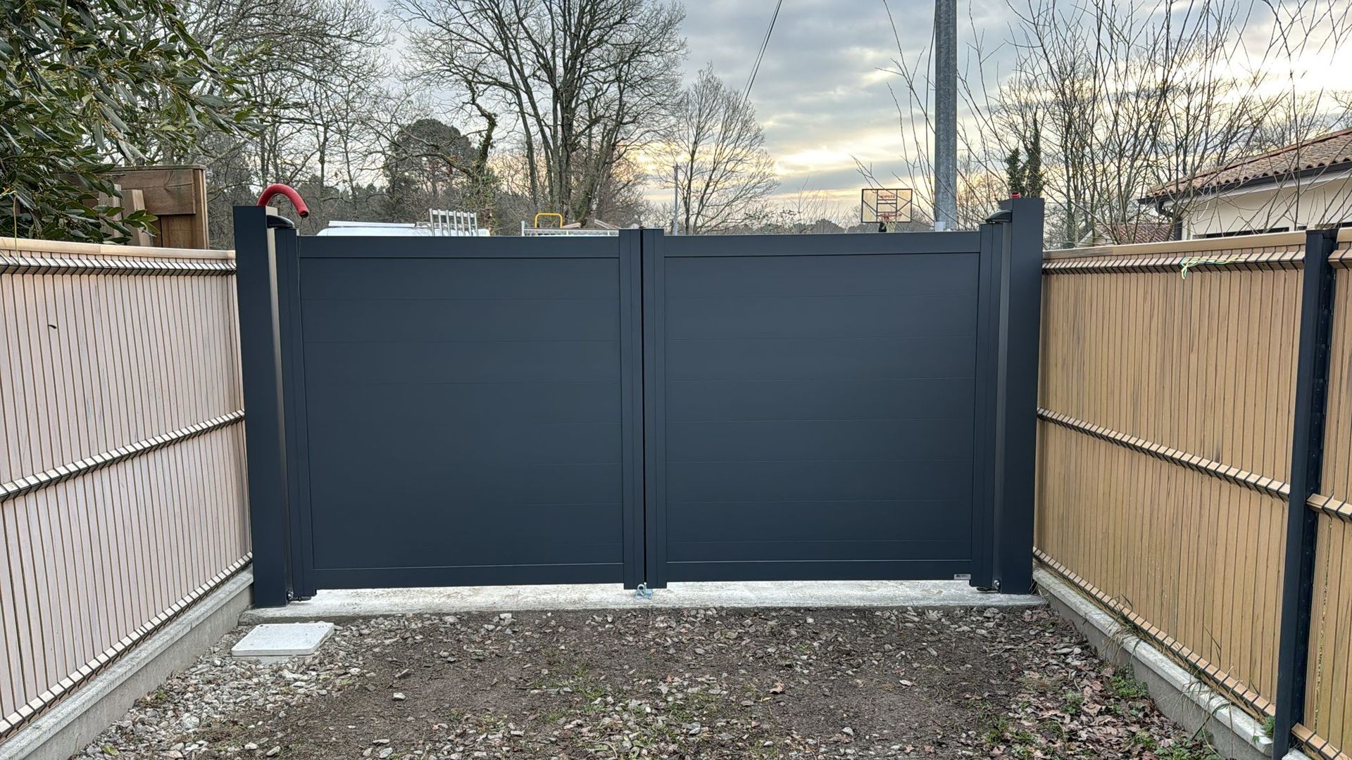 Portail double gris foncé entre des clôtures en bambou beige.