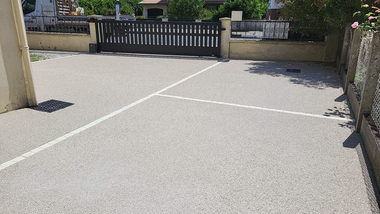 Allée de gravier avec lignes blanches menant à un portail sombre. Des murs bordent l'allée.