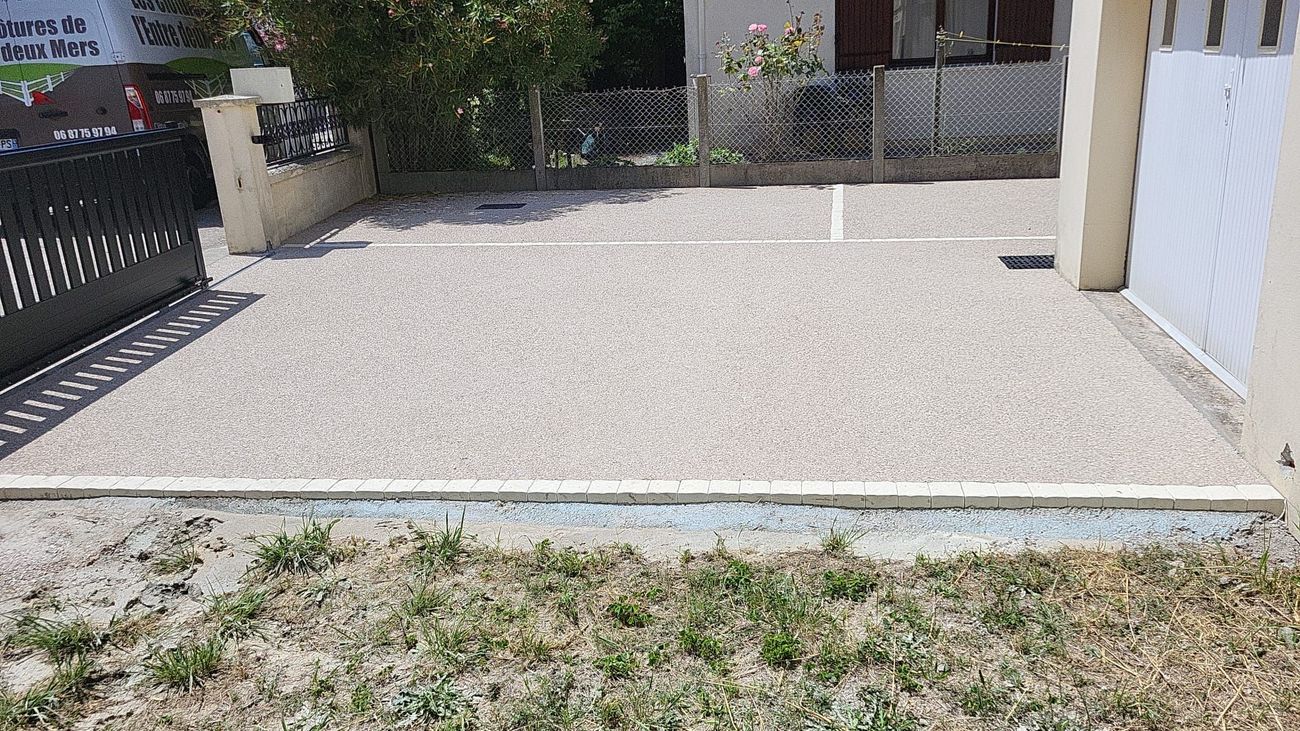 Allée en gravier bordée de béton, à côté d'un bâtiment et d'une entrée fermée par un portail.