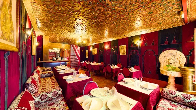 Salle à manger luxueuse rouge et or avec tables basses, coussins, plafond orné et éclairage d'ambiance chaleureux