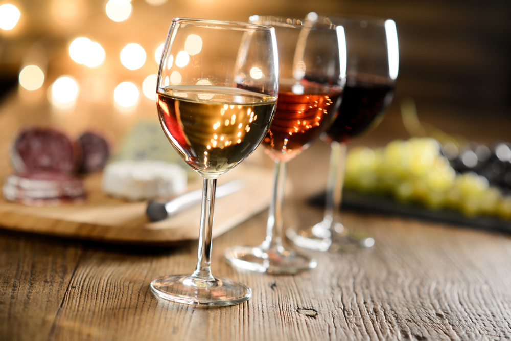 Deux verres de rosé sur une table rustique, avec du fromage et des raisins légèrement flous en arrière-plan.