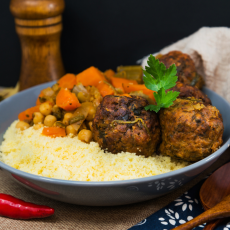 Bol de couscous avec ragoût de pois chiches et légumes et boulettes de viande dorées, garni de persil
