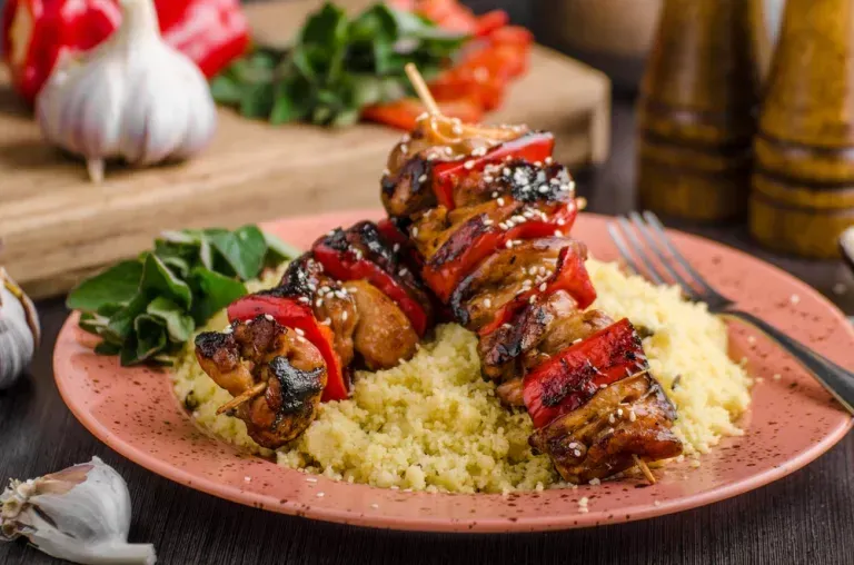 Brochettes grillées aux poivrons rouges servies sur du couscous dans une assiette rose