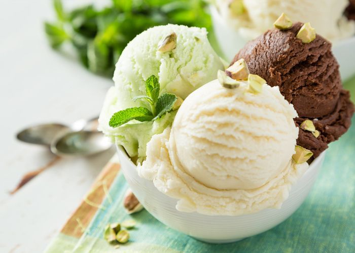 Trois boules de glace dans un bol, avec des feuilles de menthe et des pistaches sur une surface blanche