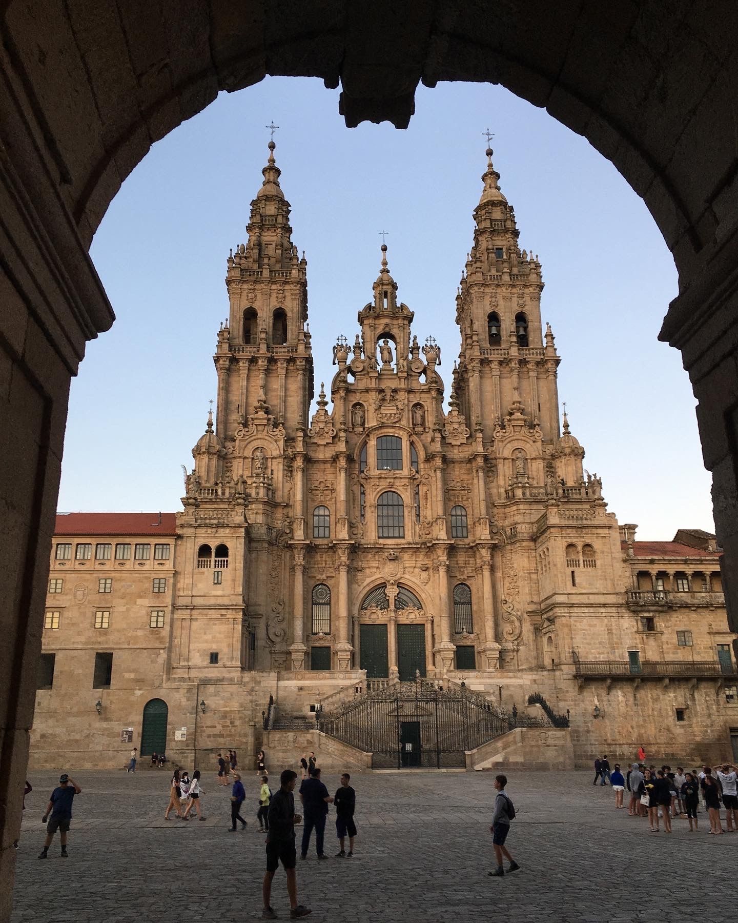 Fachada de la catedral enmarcada por un arco, con gente en la plaza de abajo bajo un cielo azul.