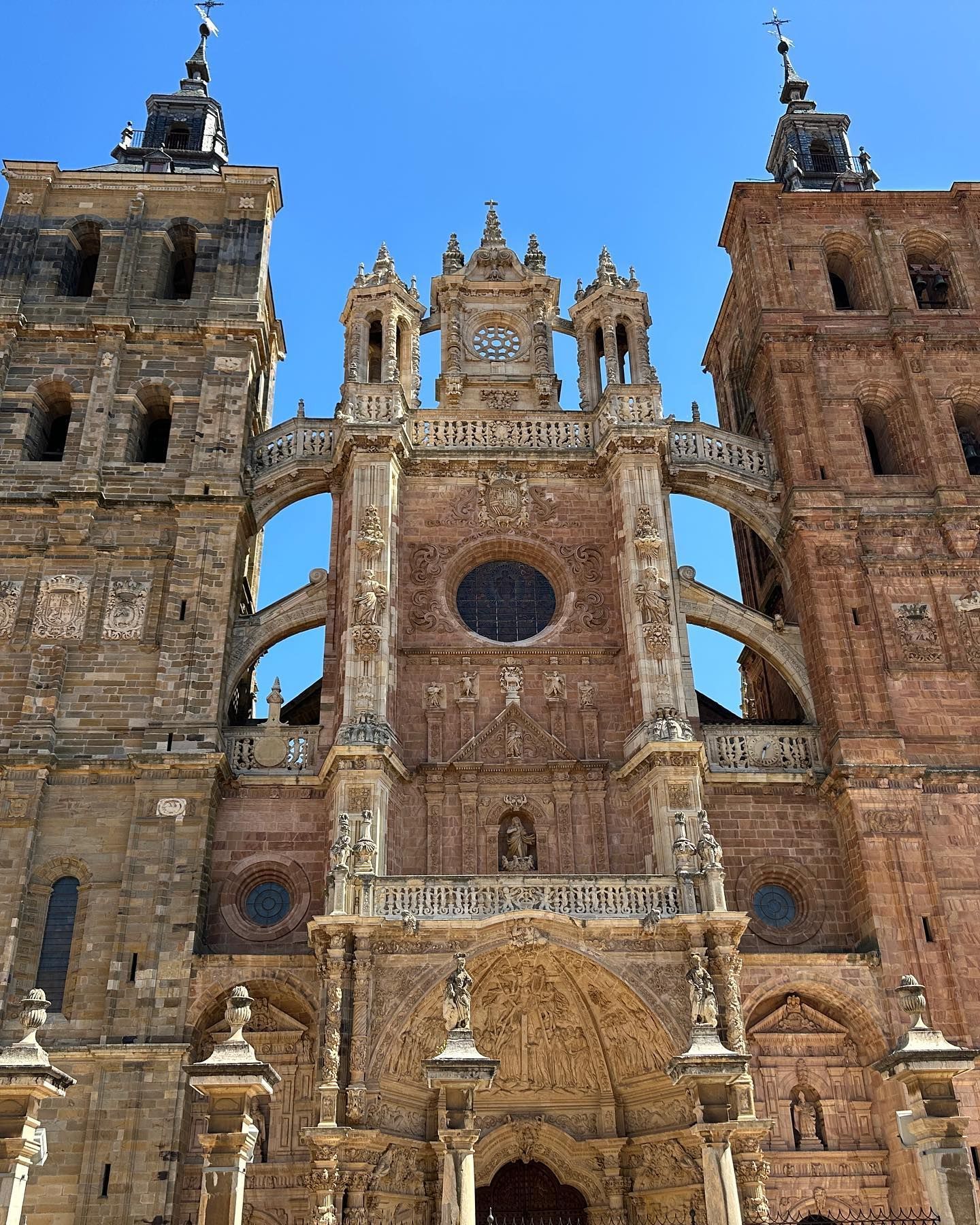 Fachada de catedral de piedra ornamentada con torres gemelas y rosetón central contra un cielo azul.