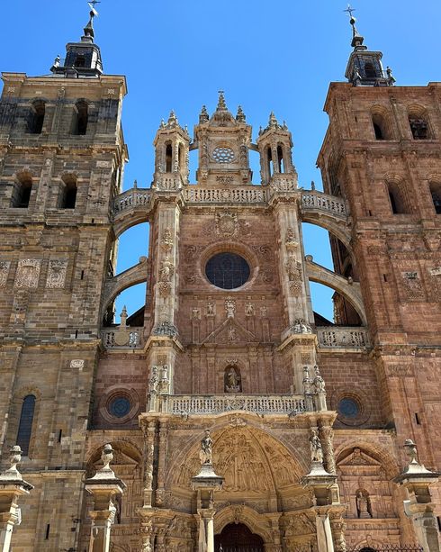Fachada de catedral de piedra ornamentada con torres gemelas y rosetón central contra un cielo azul.