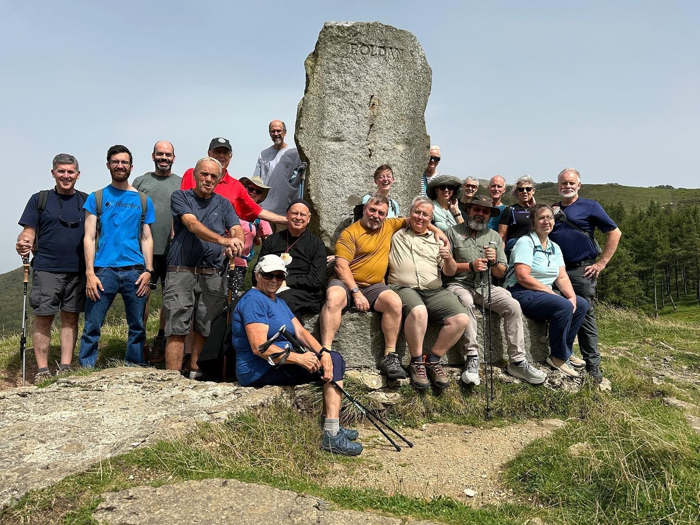 Grupo de excursionistas posando en la cima de una colina rocosa junto a una ruina de piedra bajo un cielo despejado.