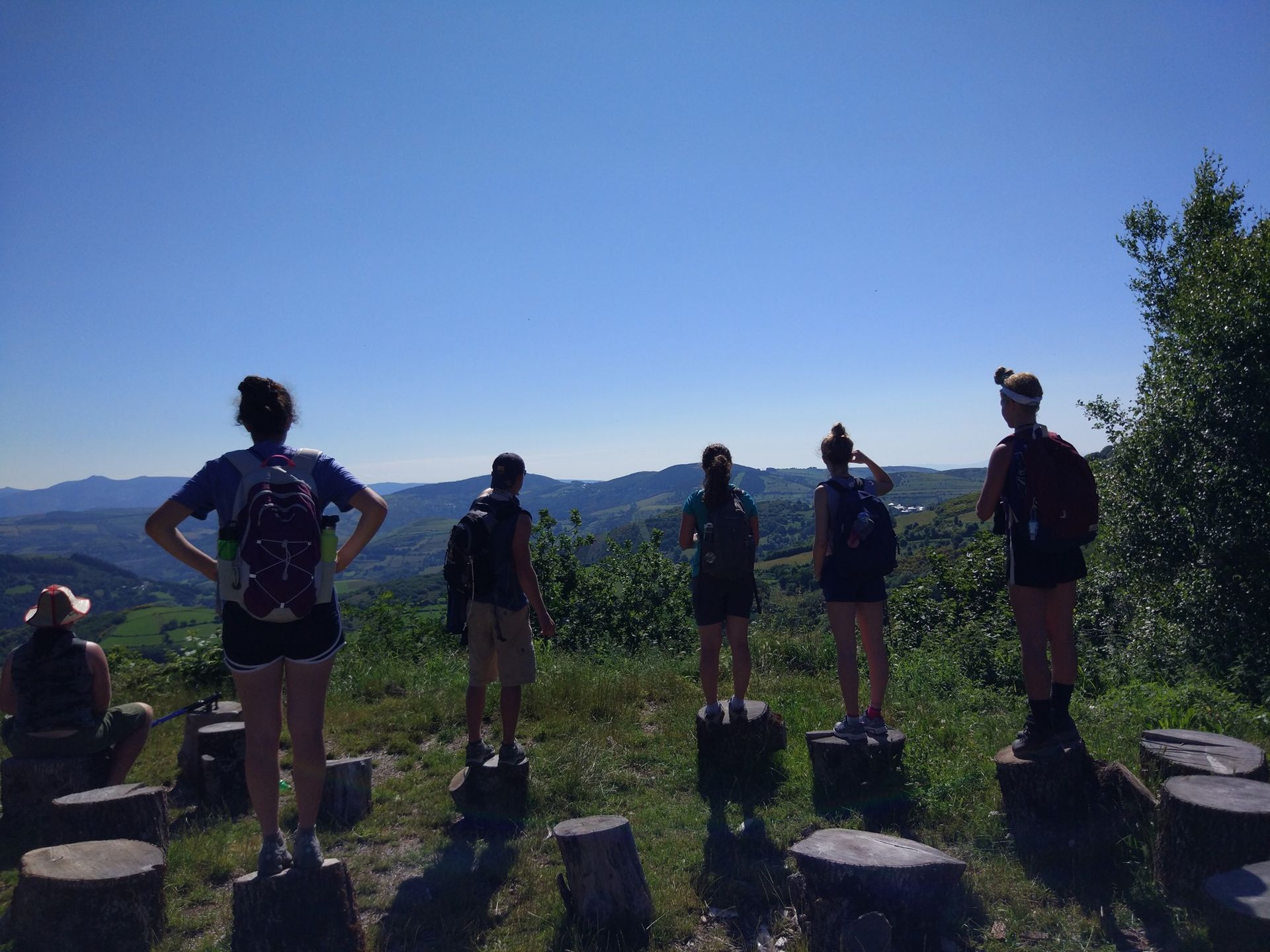 Grupo de excursionistas de pie en un sendero en la cima de una colina con vistas a la montaña y cielo azul al fondo.