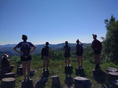 Grupo de excursionistas de pie en un sendero en la cima de una colina con vistas a la montaña y cielo azul al fondo.