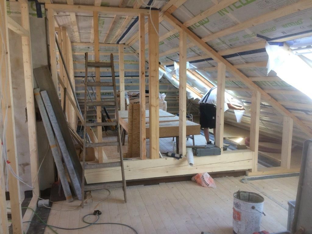 Ein Mann steht mit einer Leiter auf einem Dachboden im Rohbau.