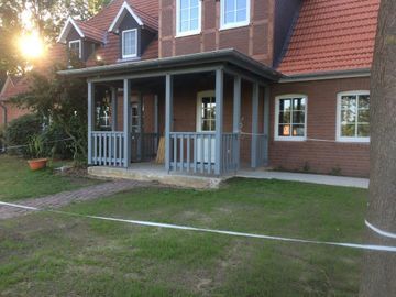 Ein Backsteinhaus mit einer Veranda und einem Baum davor.