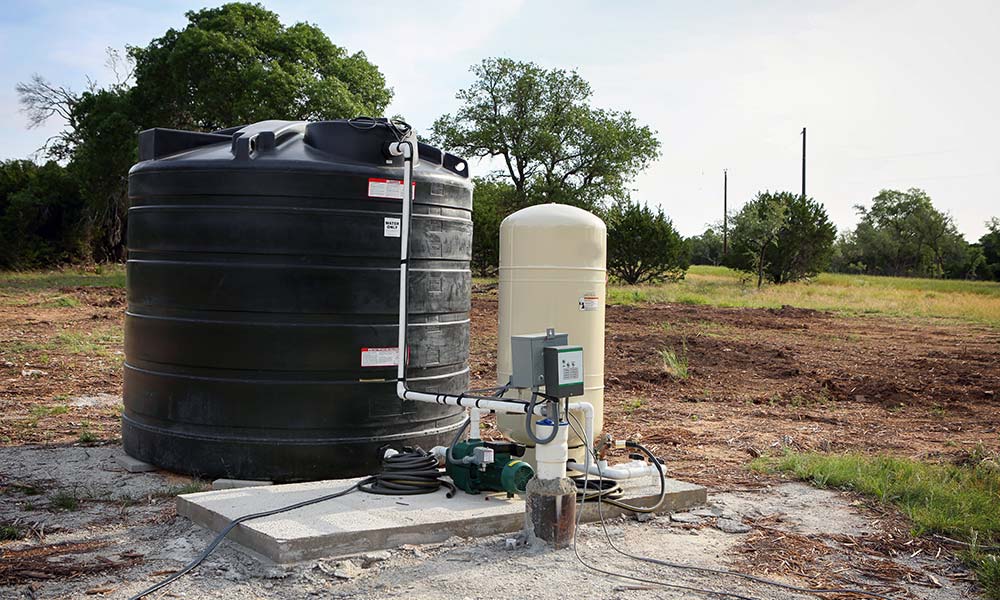 Réservoir d'eau noir posé à côté d'une dalle de béton dans un sol de terre