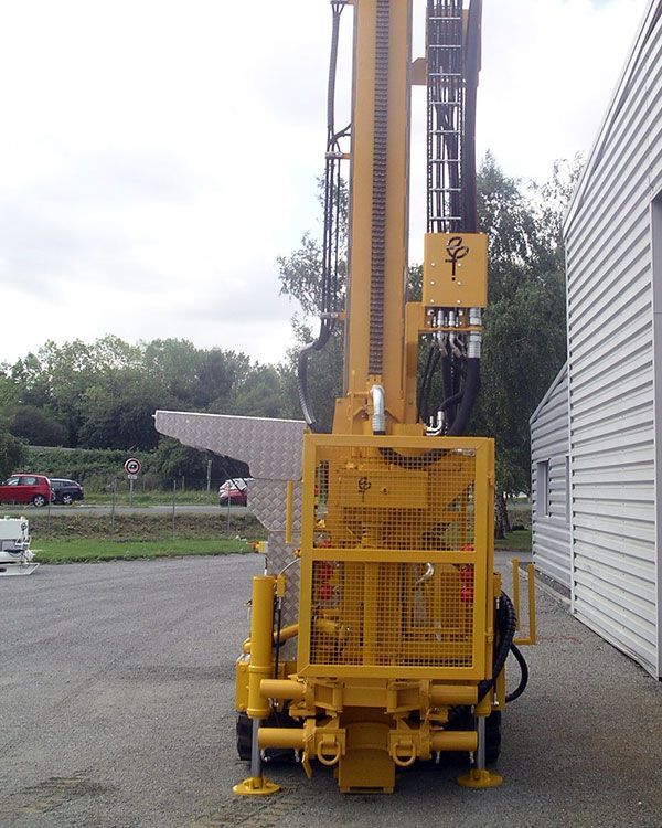 Véhicule jaune de forage posé sur le bitume devant un bâtiment en tôle