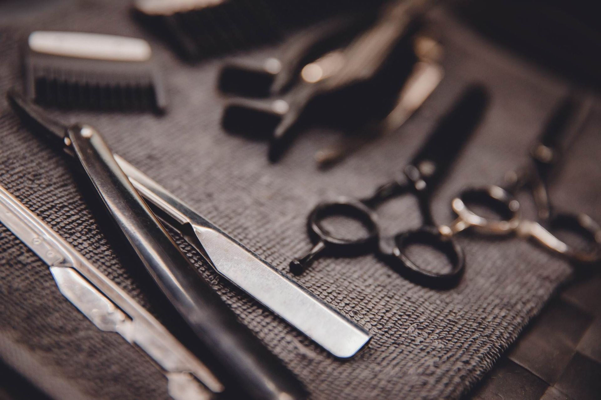 Herramientas de barbería sobre un paño texturizado: tijeras, peine, navaja de afeitar y maquinilla de cortar pelo.