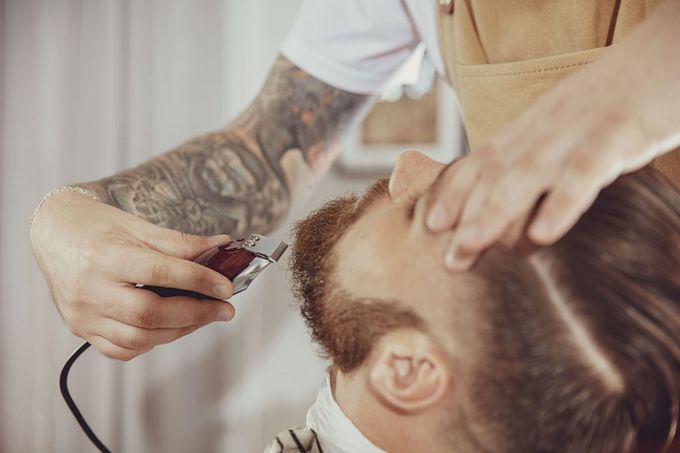 Un barbero recorta la barba de un cliente con una maquinilla eléctrica en un salón de belleza.
