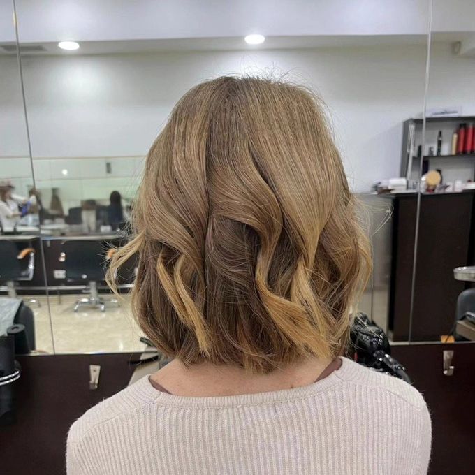 Espalda de una persona con cabello rubio ondulado hasta los hombros en un espejo de peluquería.
