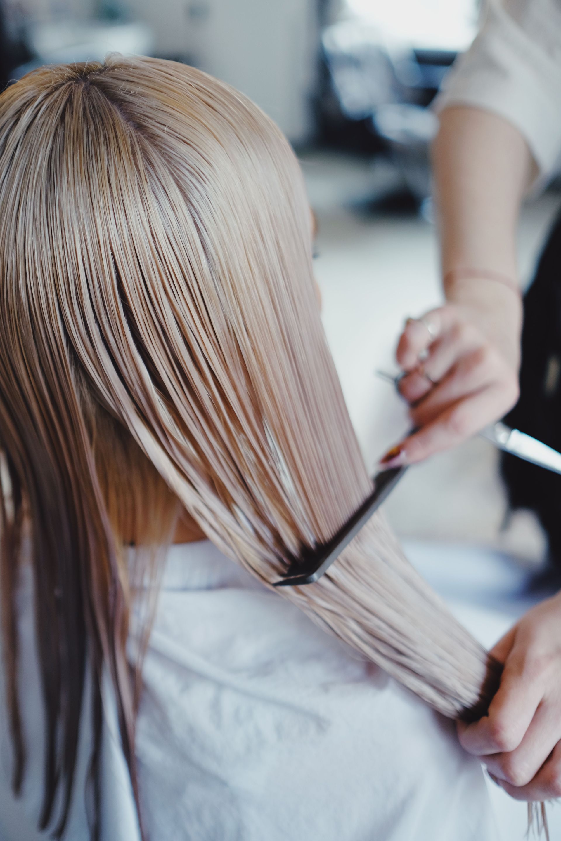 Peluquera separando el cabello con un peine negro y pinzas en un salón de belleza.