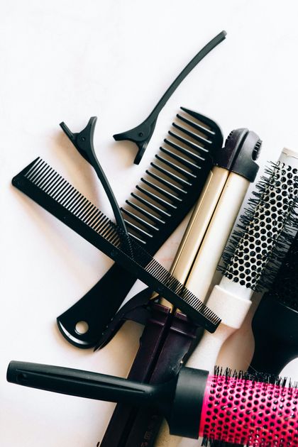 Variedad de herramientas y peines para peinar el cabello sobre un fondo blanco, incluyendo cepillos, peines y pinzas.