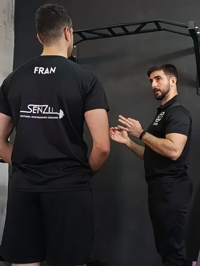 Dos hombres están parados uno al lado del otro en un gimnasio hablando entre sí.
