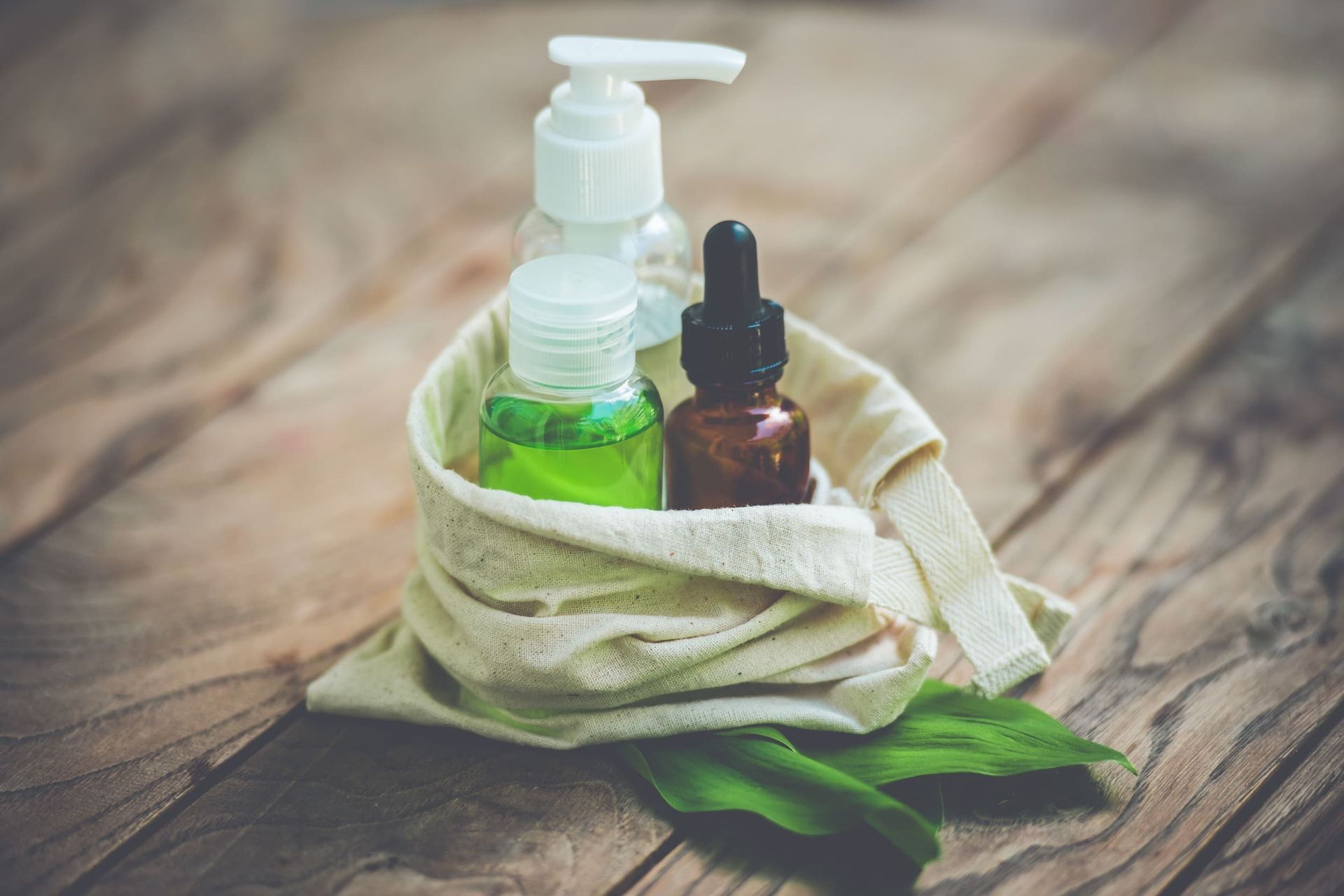 Una bolsa llena de botellas de cosméticos y hojas sobre una mesa de madera.