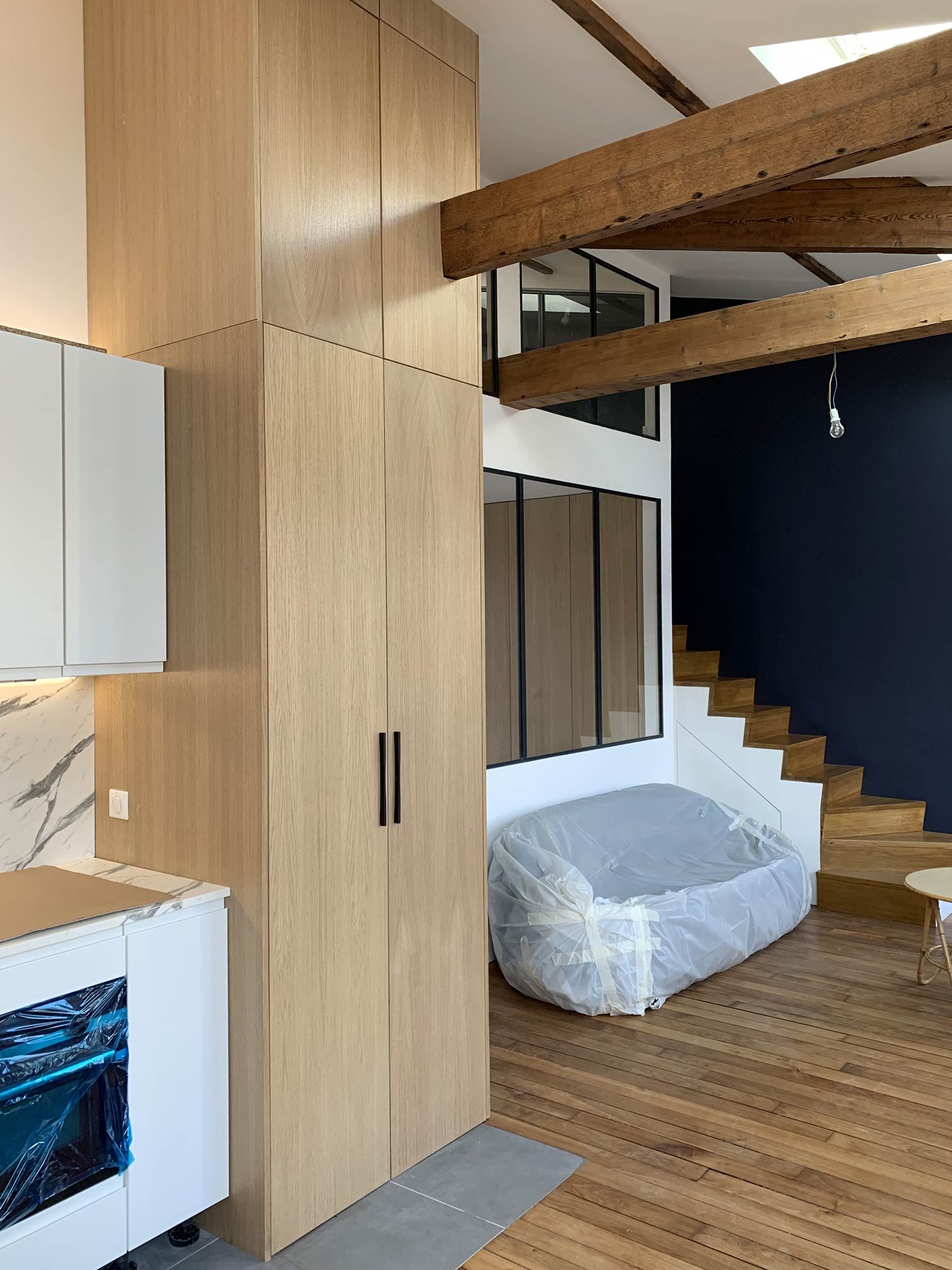 Salon aménagé avec poutres apparentes et verrières industrielles