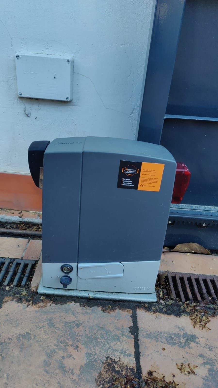 Caja eléctrica industrial gris montada junto a una pared azul, sobre un suelo de hormigón mojado.