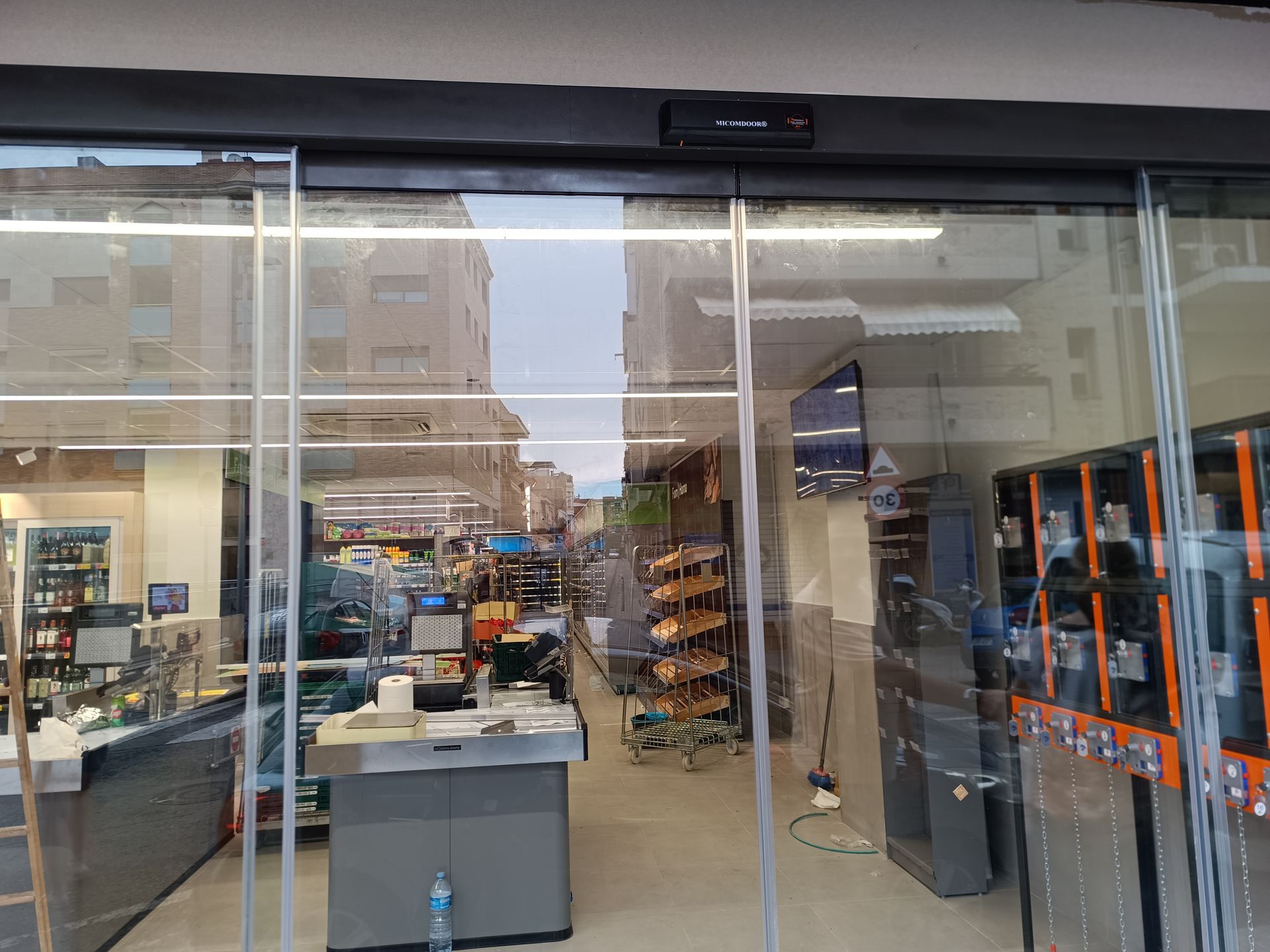 Entrada de una tienda con puertas de cristal, a través de las cuales se ven estanterías y expositores en el interior