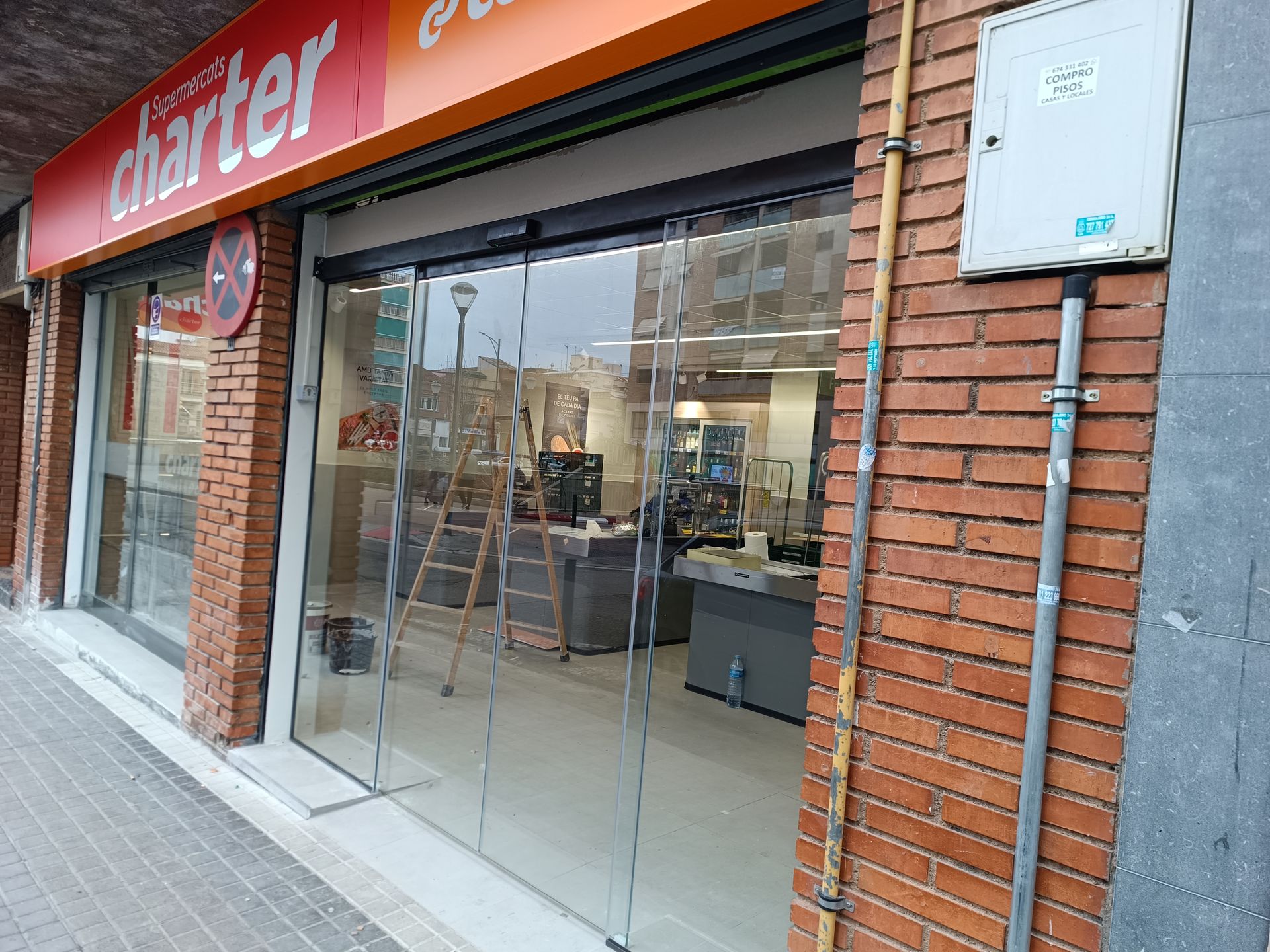 Local con puertas de cristal y un letrero naranja en una esquina adoquinada