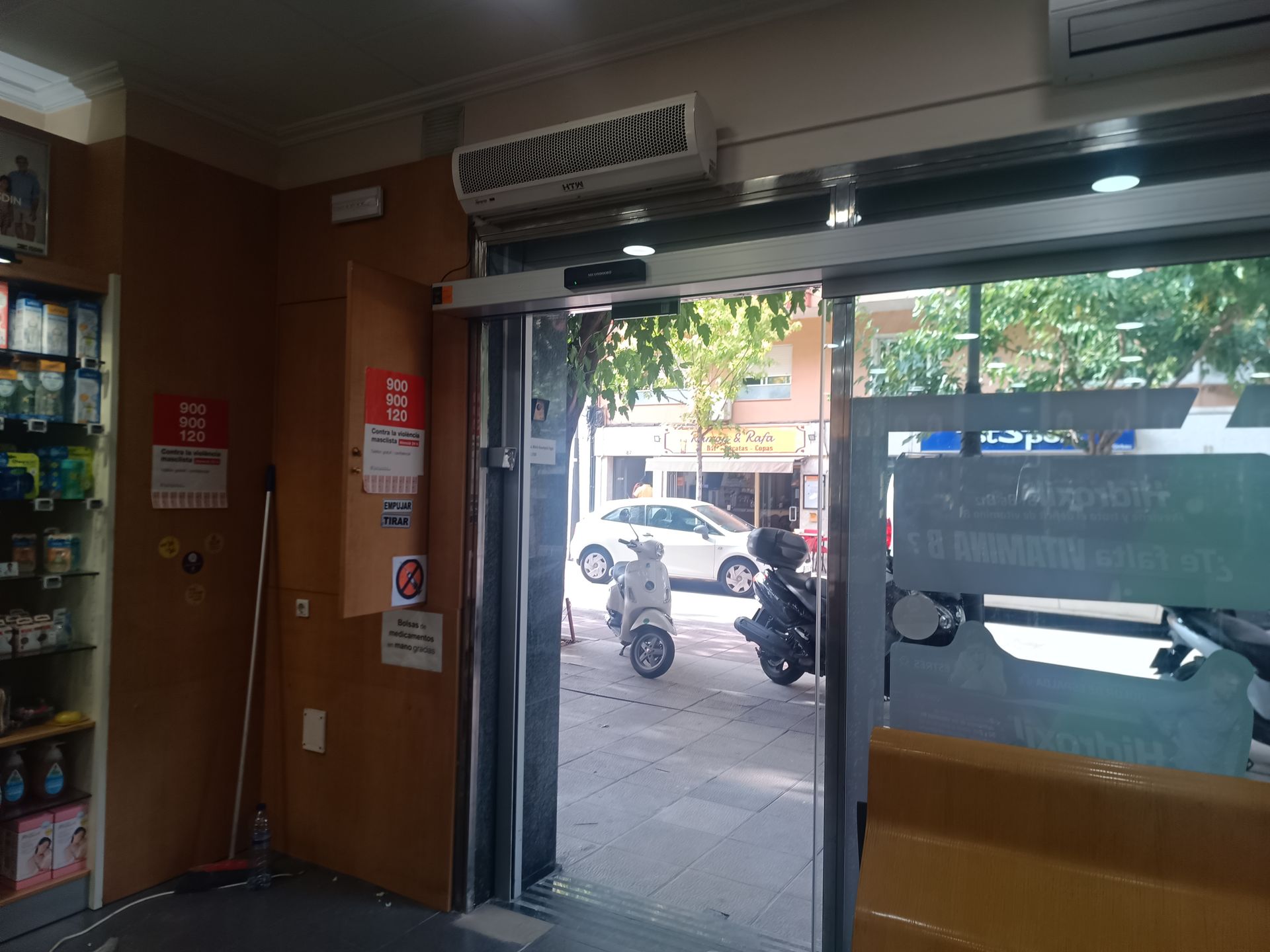 Entrada de la tienda con las puertas de cristal abiertas, que deja ver una calle con coches aparcados.