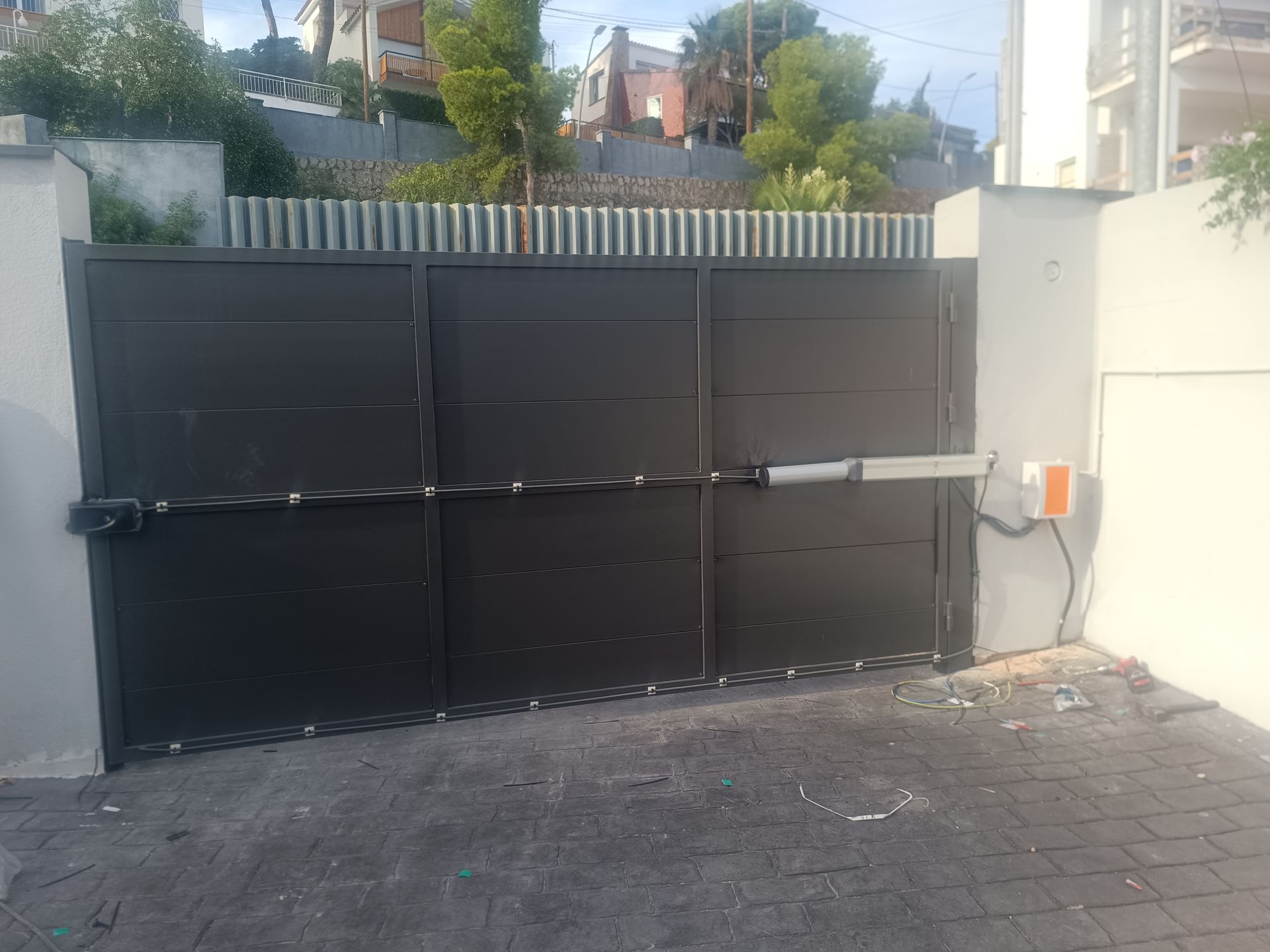Portón negro de metal para entrada de vehículos, con un teclado numérico montado en la pared
