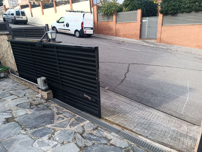 Vista a través de puertas de cristal hacia un sendero del parque, con árboles y una barandilla roja en el exterior