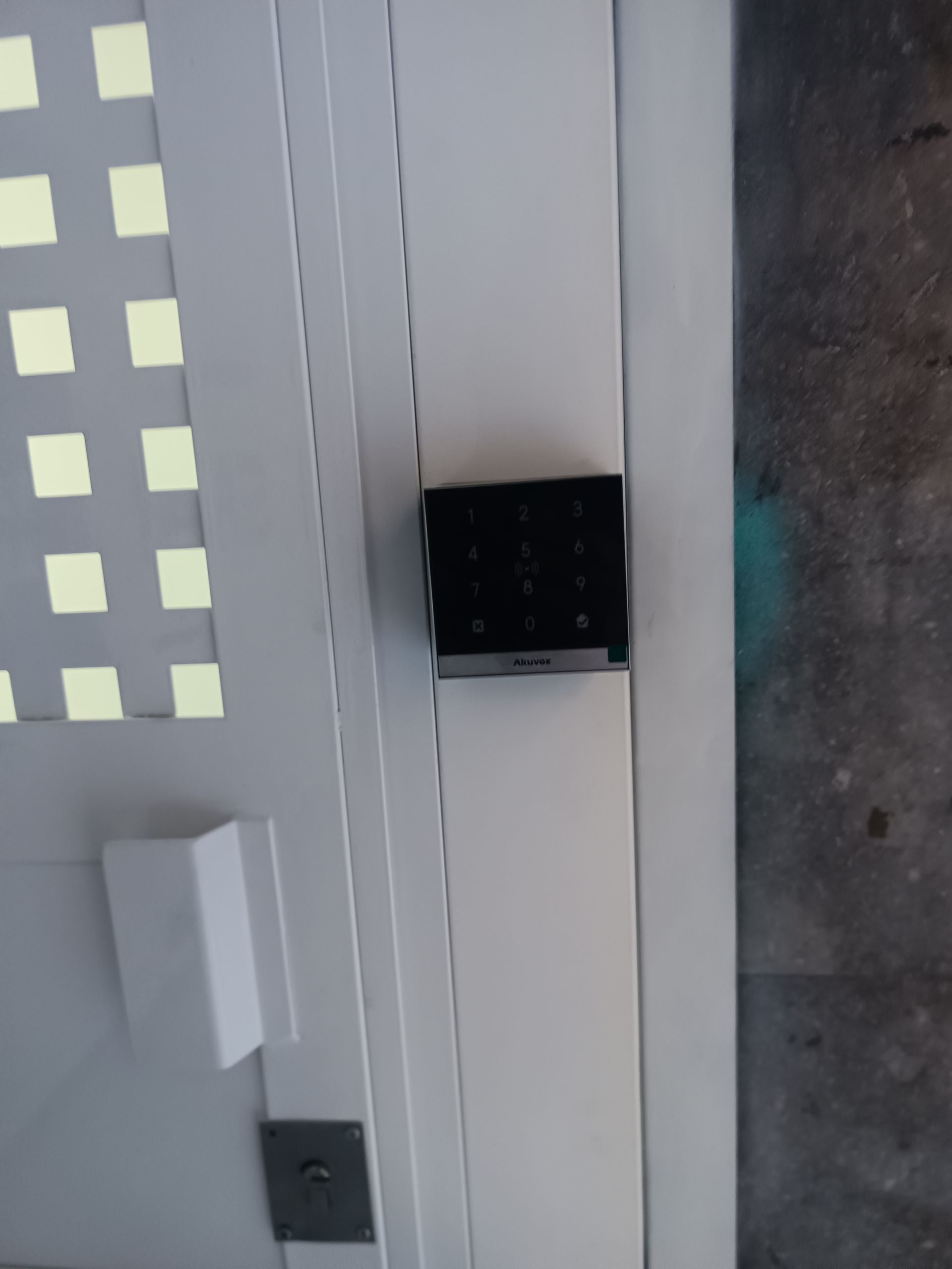 Primer plano de una pared blanca con un pequeño dispositivo negro montado cerca del centro y un suelo gris al lado.