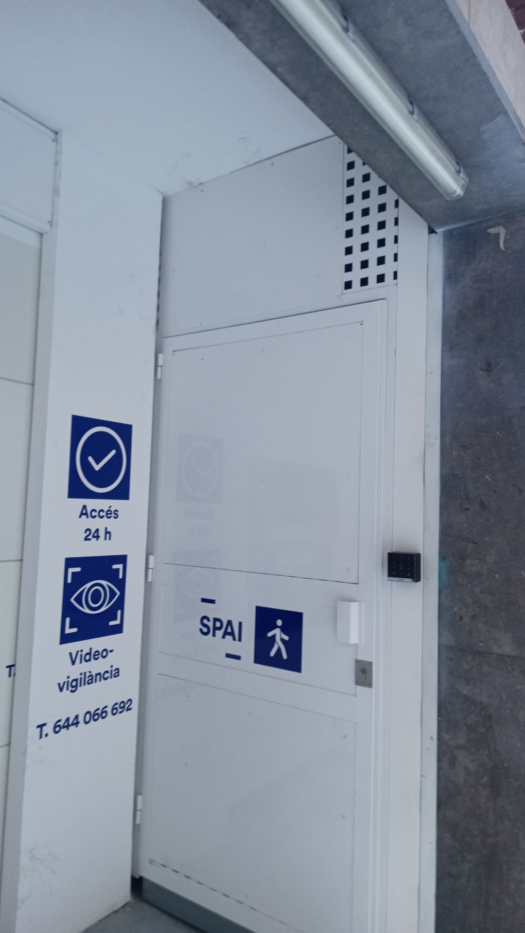 Puerta blanca de emergencia en un pasillo de hormigón con señales azules de accesibilidad y salida.