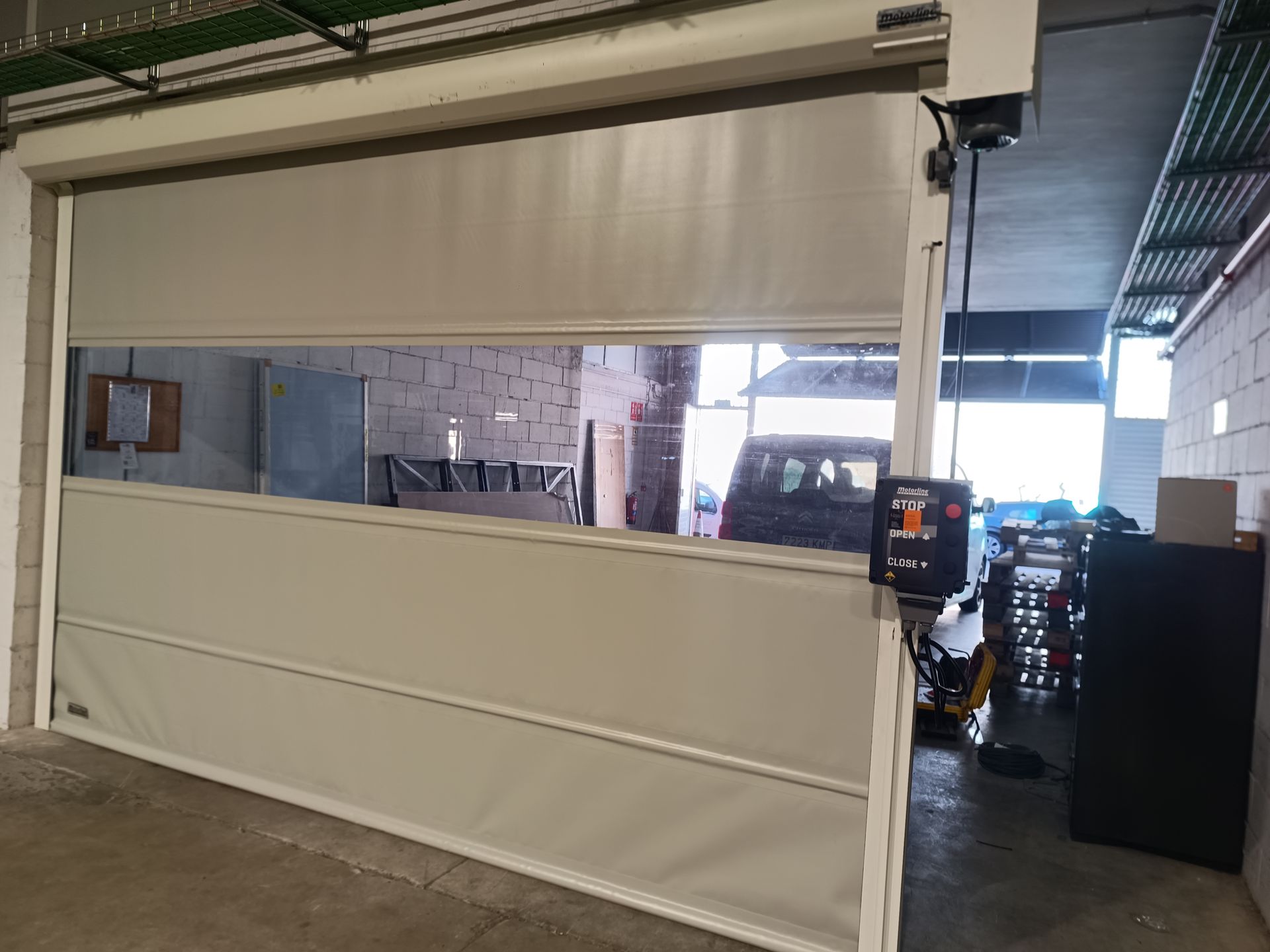 Puerta industrial de garaje con una gran ventana rectangular que da al interior de un almacén.