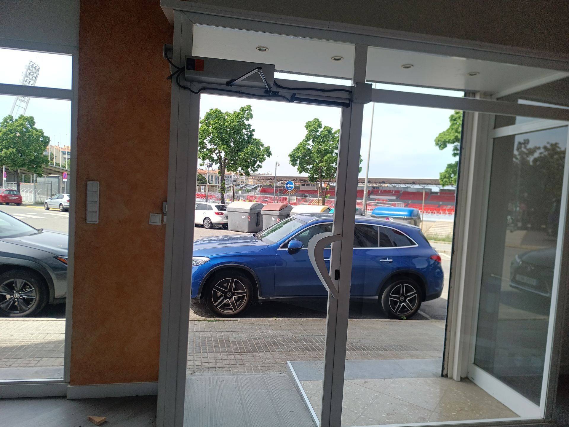 Un SUV azul estacionado frente a un local, visto a través de una entrada de cristal.