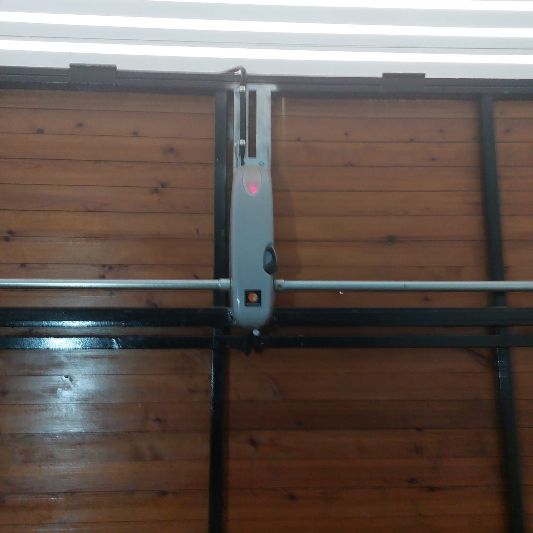 Abridor de puerta de garaje montado en un techo de madera, con una pequeña luz indicadora roja.