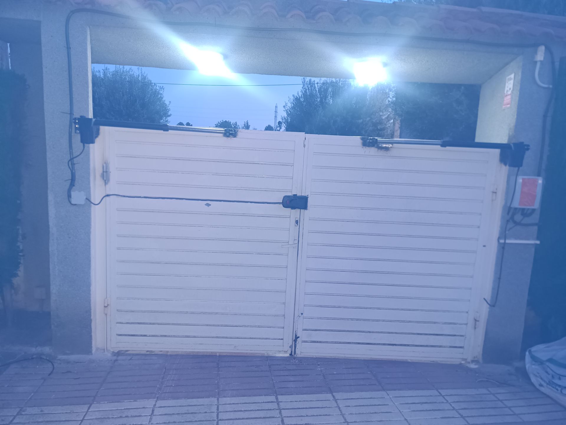 Doble puerta blanca que bloquea la entrada de un garaje, bajo la abertura de una cochera
