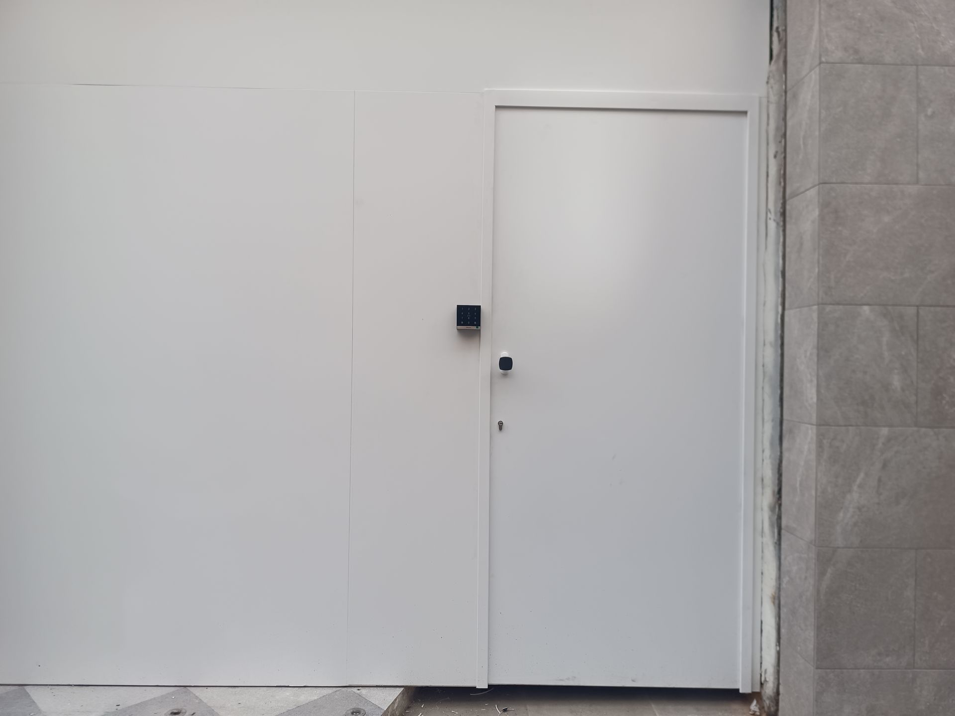 Pared blanca y puerta con un pequeño teclado numérico negro al lado, en un interior sencillo